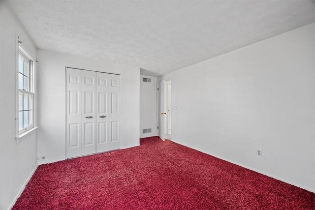 unfurnished bedroom featuring a closet, carpet flooring, a textured ceiling, and visible vents