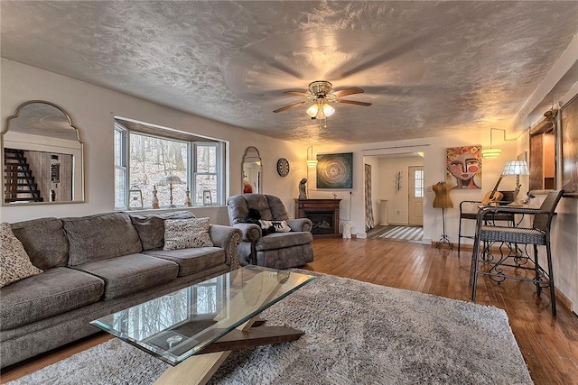 living room featuring a ceiling fan, hardwood / wood-style flooring, a textured ceiling, a fireplace, and baseboards