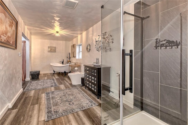 full bath featuring wood finished floors, visible vents, baseboards, a freestanding tub, and a shower stall