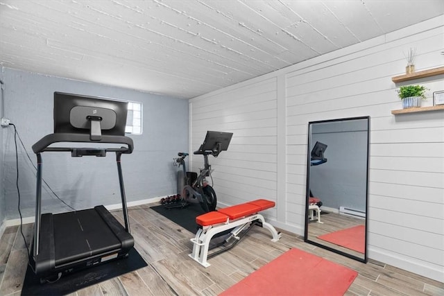 workout area featuring wooden walls, a baseboard heating unit, baseboards, and wood finished floors