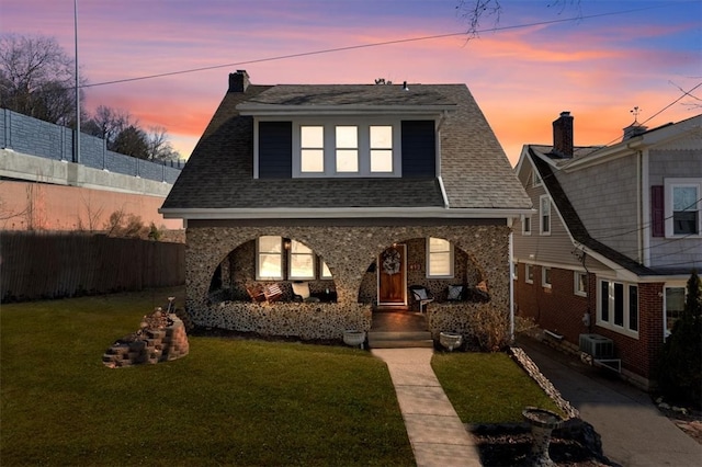 view of front of house with a lawn, a porch, fence, a shingled roof, and a chimney