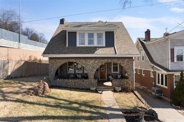 view of front facade featuring a porch, fence, a front lawn, and roof with shingles