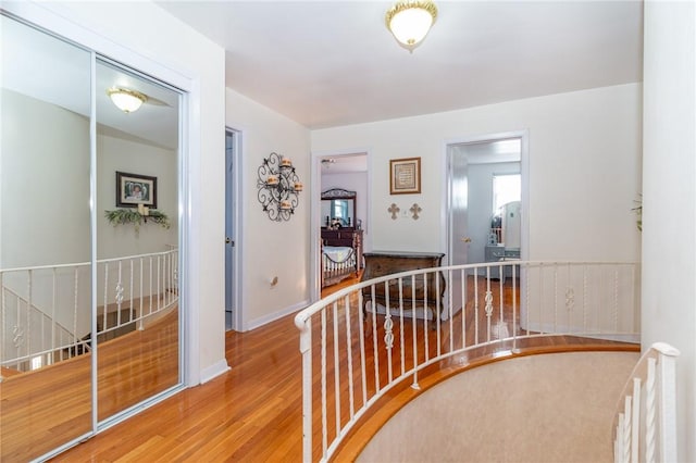 corridor featuring wood finished floors, an upstairs landing, and baseboards