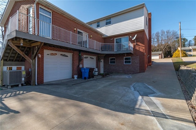 rear view of property with a garage, brick siding, cooling unit, and driveway