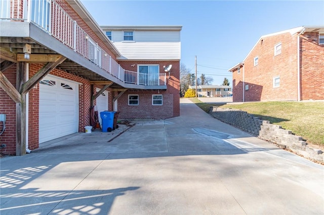view of side of home with brick siding, a balcony, driveway, and a garage