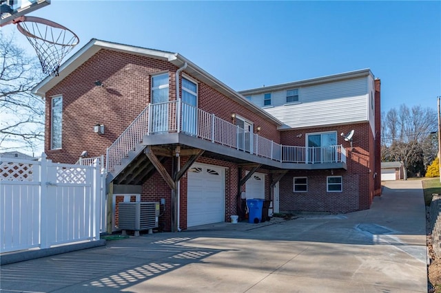 rear view of property featuring brick siding, an attached garage, concrete driveway, and fence