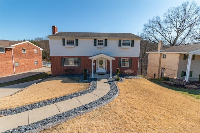 colonial home featuring a front yard, brick siding, and a chimney