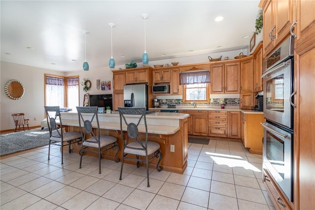 kitchen with a breakfast bar, a kitchen island, appliances with stainless steel finishes, light countertops, and light tile patterned floors