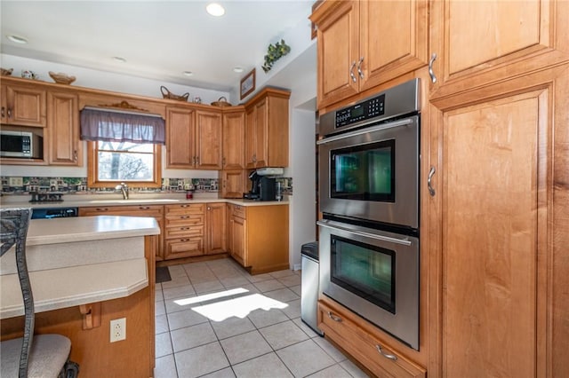 kitchen featuring a breakfast bar, light countertops, appliances with stainless steel finishes, light tile patterned flooring, and a sink