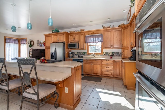 kitchen with a breakfast bar, light countertops, appliances with stainless steel finishes, light tile patterned flooring, and a sink