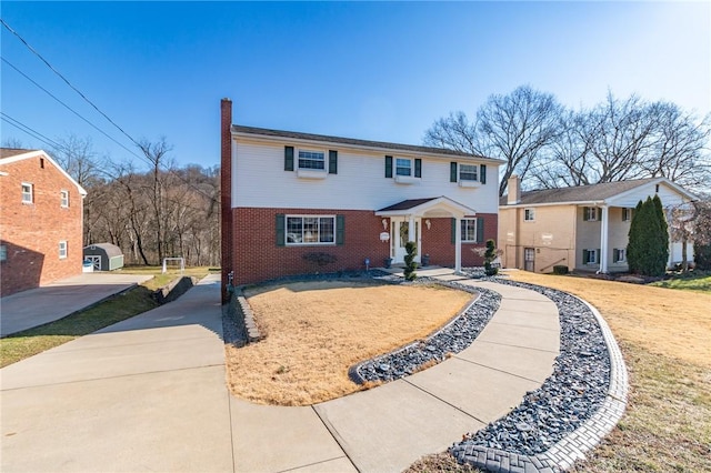 view of front of house with brick siding, driveway, and a chimney