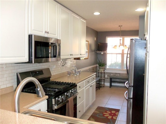 kitchen with light countertops, light tile patterned floors, appliances with stainless steel finishes, hanging light fixtures, and white cabinets