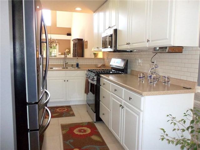 kitchen with light tile patterned flooring, a sink, decorative backsplash, appliances with stainless steel finishes, and white cabinetry