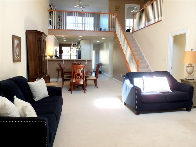 carpeted living area with ceiling fan with notable chandelier, baseboards, stairs, and a towering ceiling