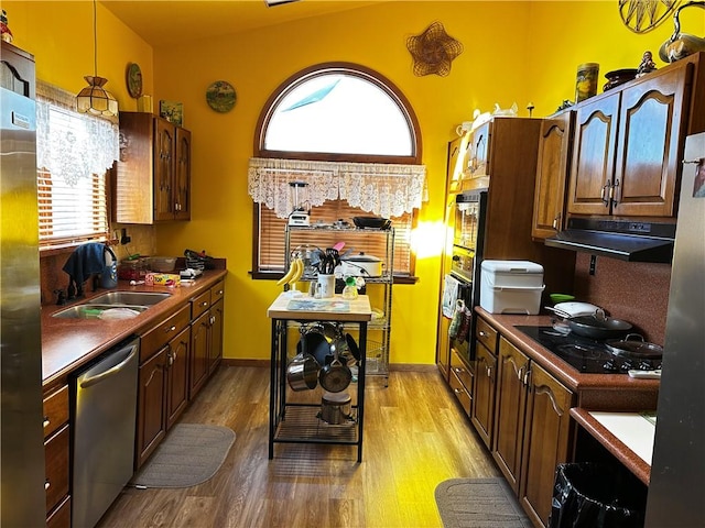 kitchen with black appliances, under cabinet range hood, a sink, light wood finished floors, and baseboards