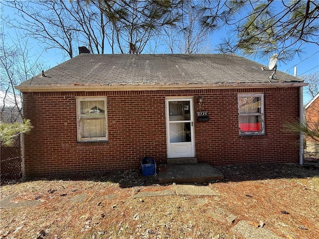 rear view of house featuring brick siding, a chimney, fence, and a shingled roof