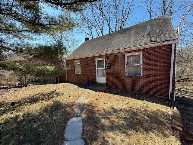 rear view of house featuring brick siding and a shingled roof