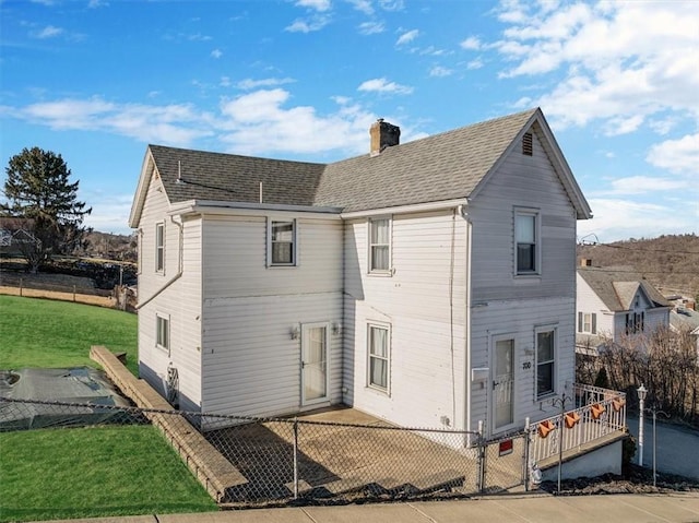 rear view of house with roof with shingles, a yard, a fenced front yard, and a chimney