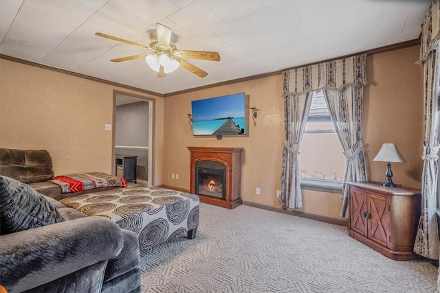 living area featuring ornamental molding, a ceiling fan, a warm lit fireplace, carpet flooring, and baseboards