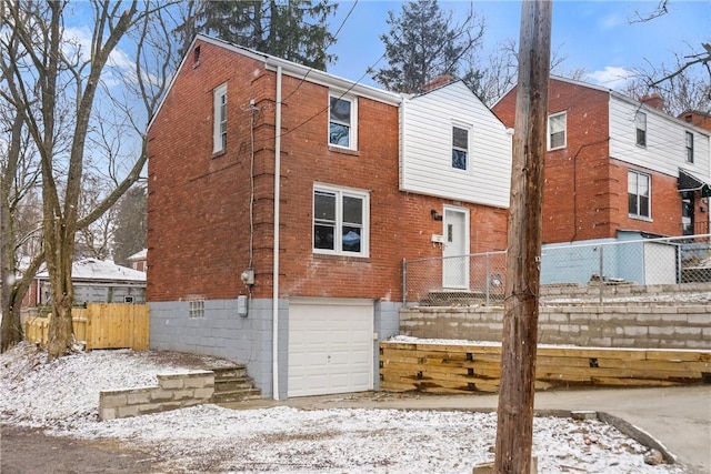 snow covered property with a garage, brick siding, and fence