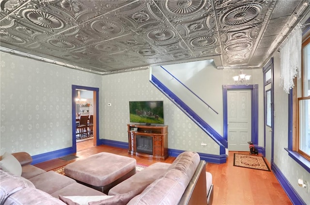 living room featuring wallpapered walls, baseboards, a chandelier, wood finished floors, and an ornate ceiling