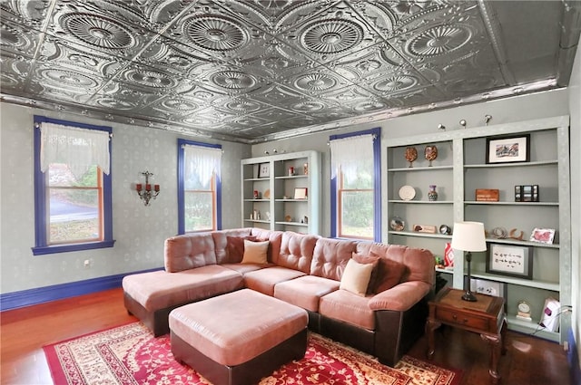 living area with an ornate ceiling, plenty of natural light, wood finished floors, wallpapered walls, and baseboards