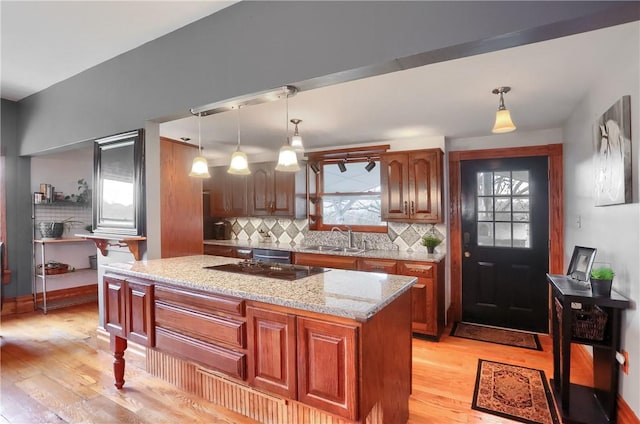 kitchen with a sink, light wood finished floors, decorative backsplash, light stone countertops, and hanging light fixtures