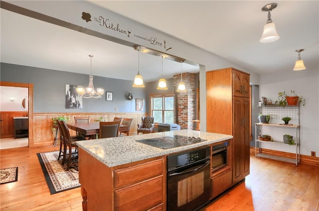 kitchen with light wood finished floors, light stone countertops, a wainscoted wall, pendant lighting, and black appliances