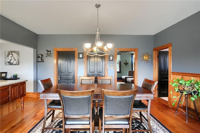 dining space with wainscoting, light wood finished floors, and a chandelier