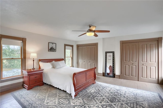 bedroom featuring light wood-style flooring, baseboards, multiple closets, and ceiling fan