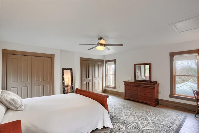 bedroom featuring two closets, light wood-style floors, baseboards, and a ceiling fan