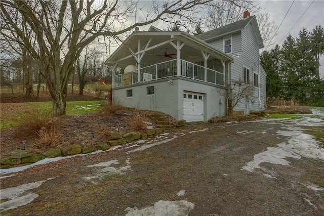 view of side of property featuring a balcony, a chimney, ceiling fan, a garage, and dirt driveway