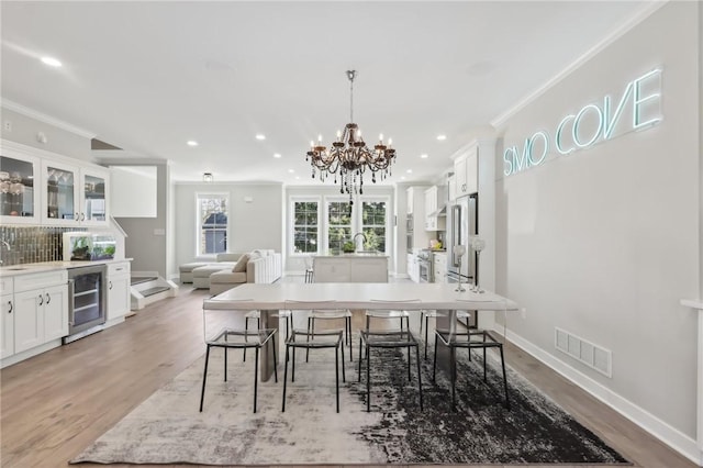 dining area with visible vents, baseboards, light wood-style flooring, wine cooler, and crown molding