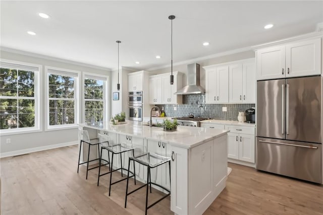 kitchen with backsplash, crown molding, wall chimney range hood, appliances with stainless steel finishes, and white cabinets