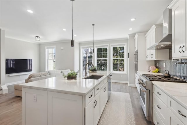 kitchen featuring a sink, stainless steel appliances, white cabinets, wall chimney range hood, and decorative backsplash