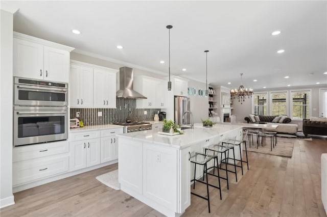 kitchen featuring stainless steel appliances, open floor plan, wall chimney exhaust hood, and white cabinets