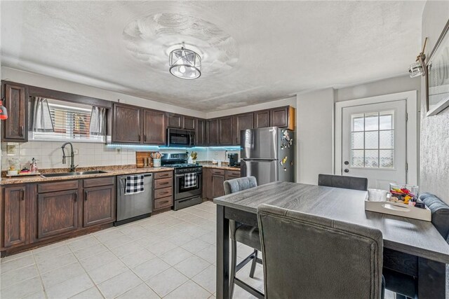 kitchen featuring a sink, light stone counters, dark brown cabinetry, appliances with stainless steel finishes, and decorative backsplash