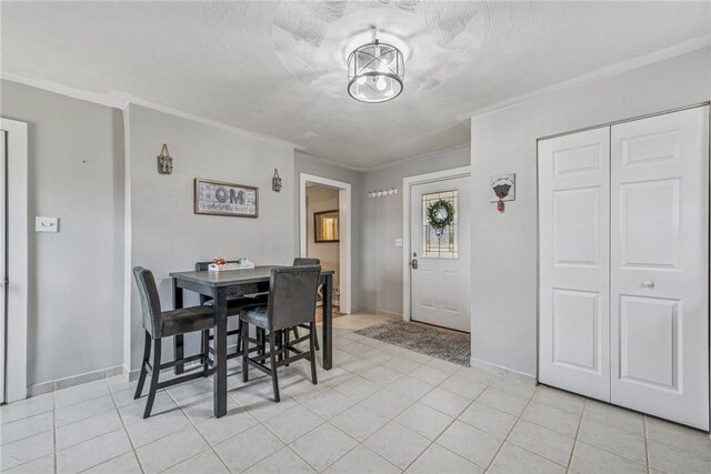 dining space featuring a textured ceiling, light tile patterned floors, baseboards, and ornamental molding