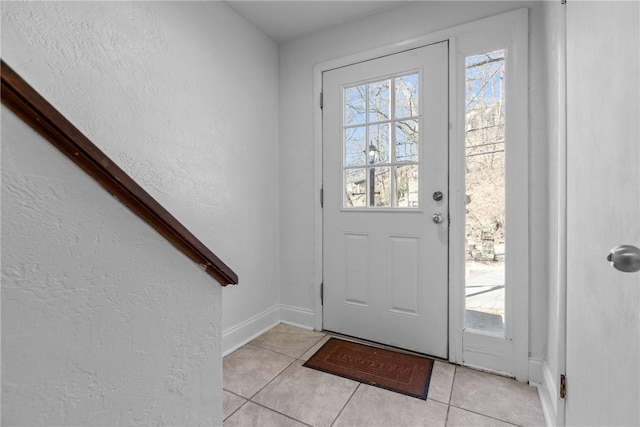 doorway with baseboards, light tile patterned flooring, and a textured wall