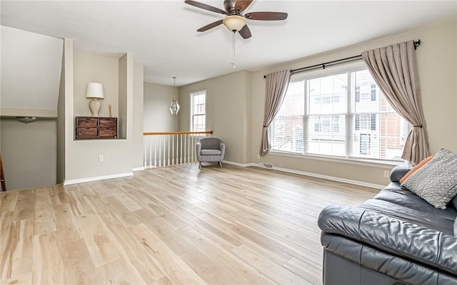 living area featuring baseboards, light wood finished floors, and ceiling fan