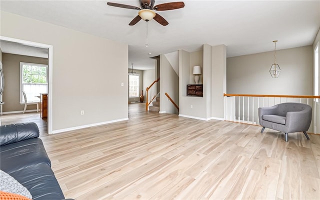 sitting room with baseboards, light wood-style flooring, and ceiling fan with notable chandelier