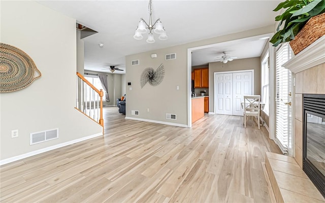 unfurnished living room with a tiled fireplace, visible vents, light wood finished floors, and stairs