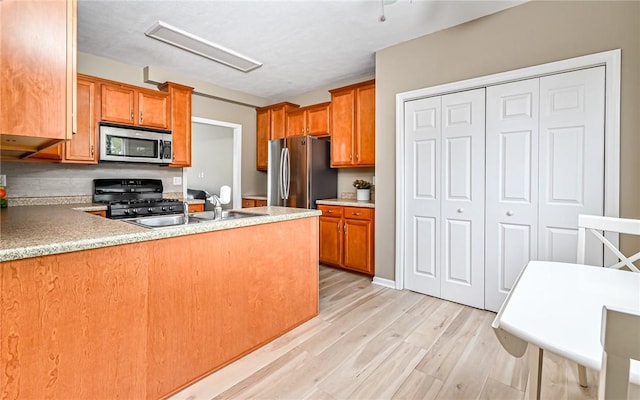 kitchen featuring brown cabinetry, light wood finished floors, a peninsula, a sink, and stainless steel appliances