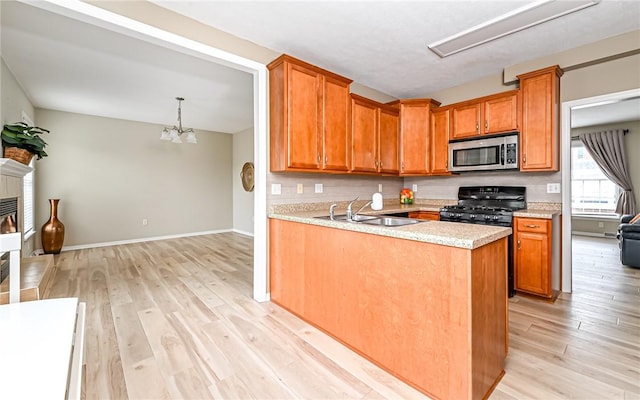 kitchen with stainless steel microwave, light wood-style floors, brown cabinetry, light countertops, and black range with gas cooktop