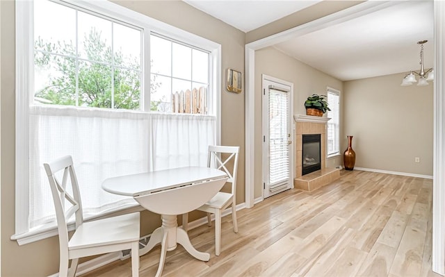 dining room featuring a notable chandelier, plenty of natural light, a fireplace, and light wood-type flooring