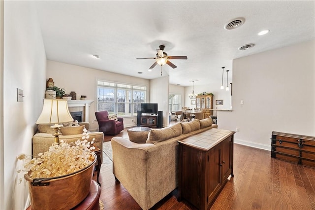 living room featuring visible vents, dark wood-type flooring, a ceiling fan, and a tile fireplace