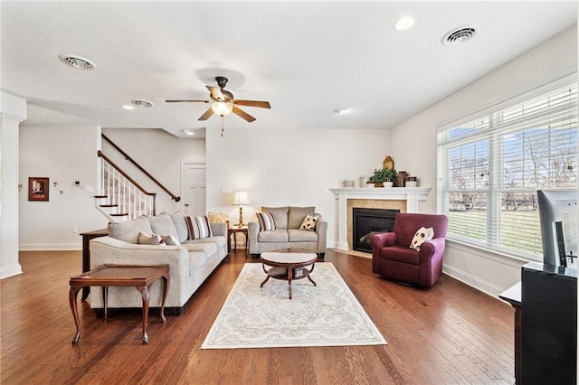 living room featuring visible vents, a fireplace with flush hearth, wood finished floors, stairway, and baseboards