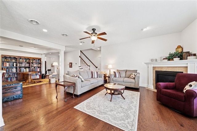 living room featuring stairway, wood finished floors, visible vents, ceiling fan, and a tiled fireplace