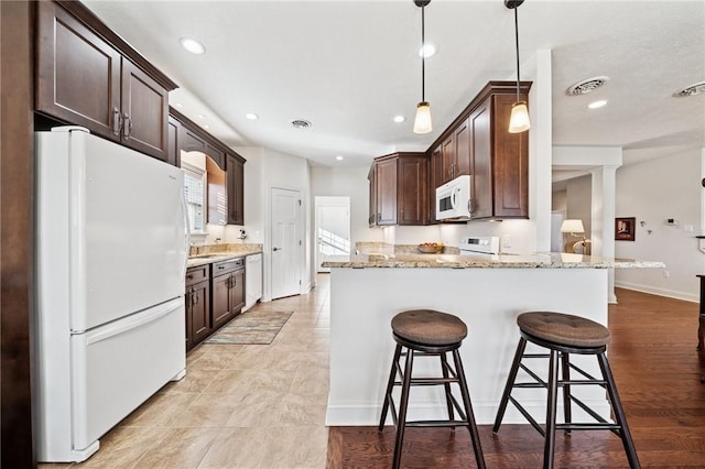 kitchen featuring visible vents, white appliances, dark brown cabinetry, and a breakfast bar