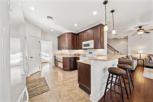 kitchen featuring visible vents, open floor plan, a breakfast bar area, light stone counters, and white appliances